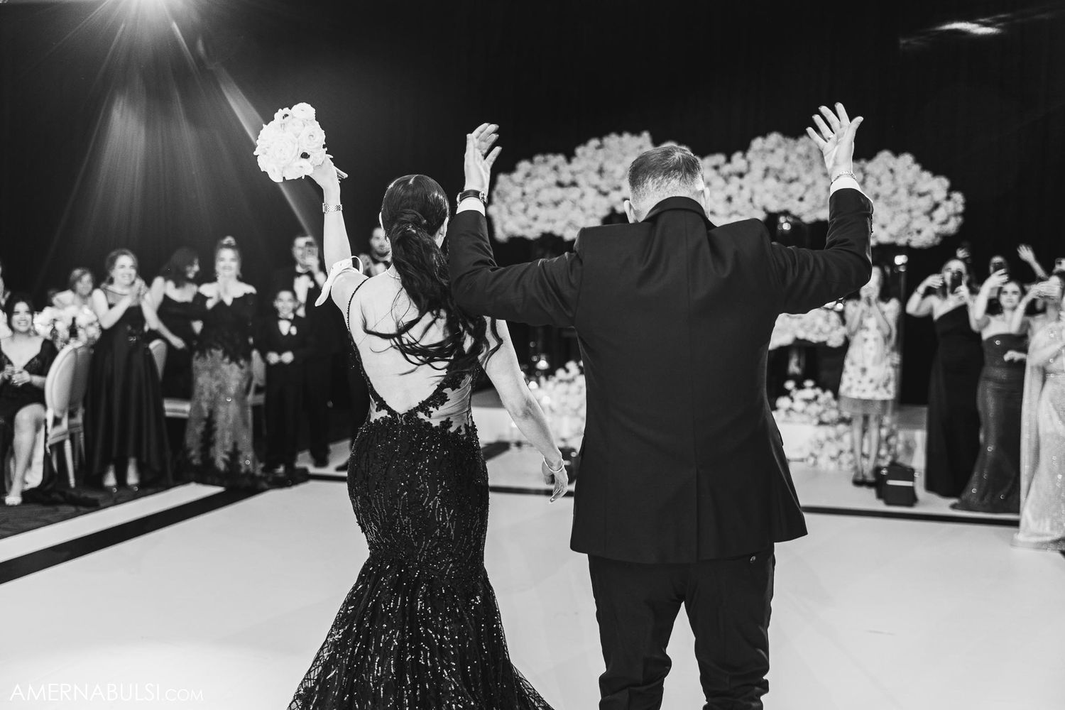 A couple celebrates on the dance floor in black formal attire during a wedding reception.