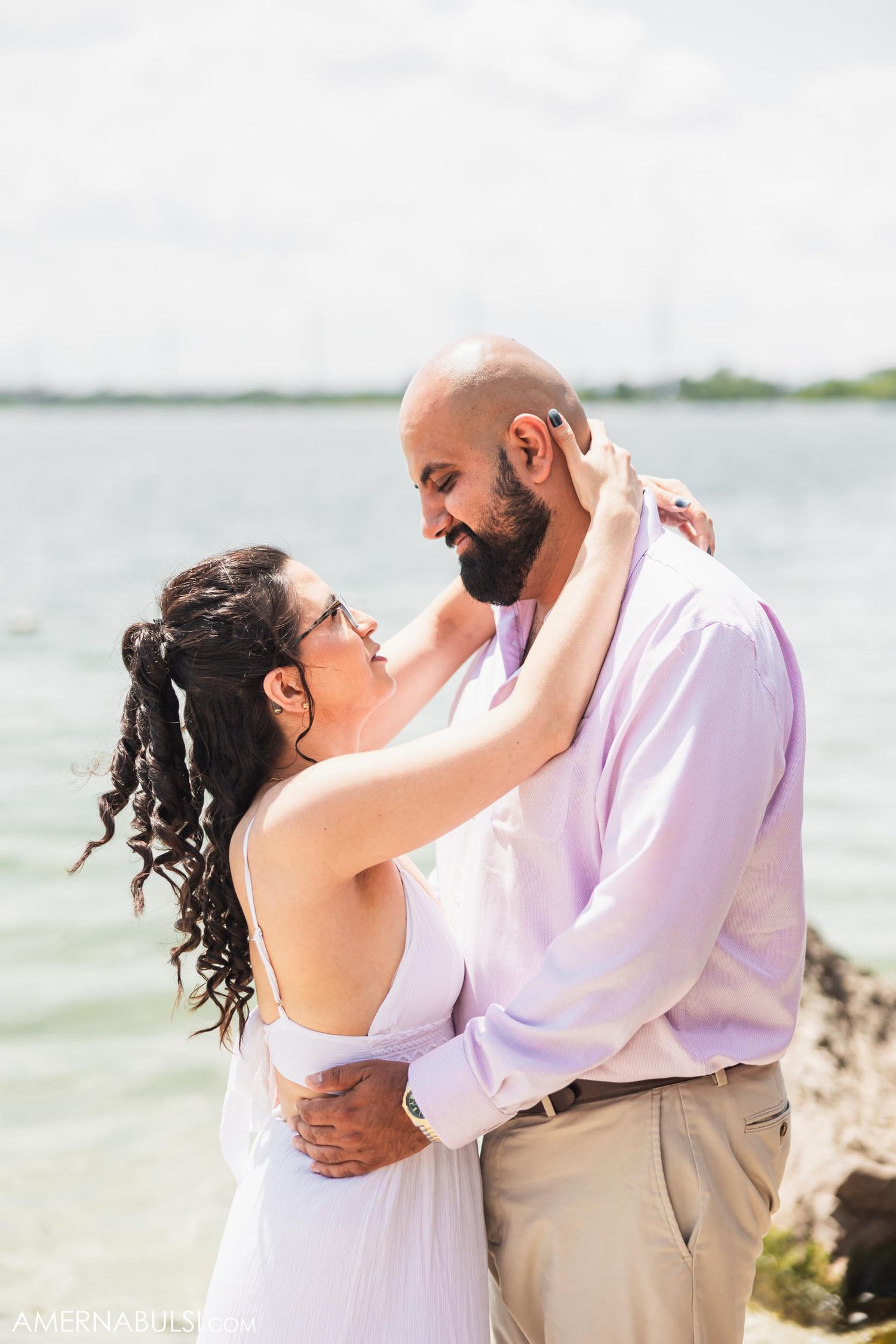 Loving couple in white and pink sharing intimate moment by the water.