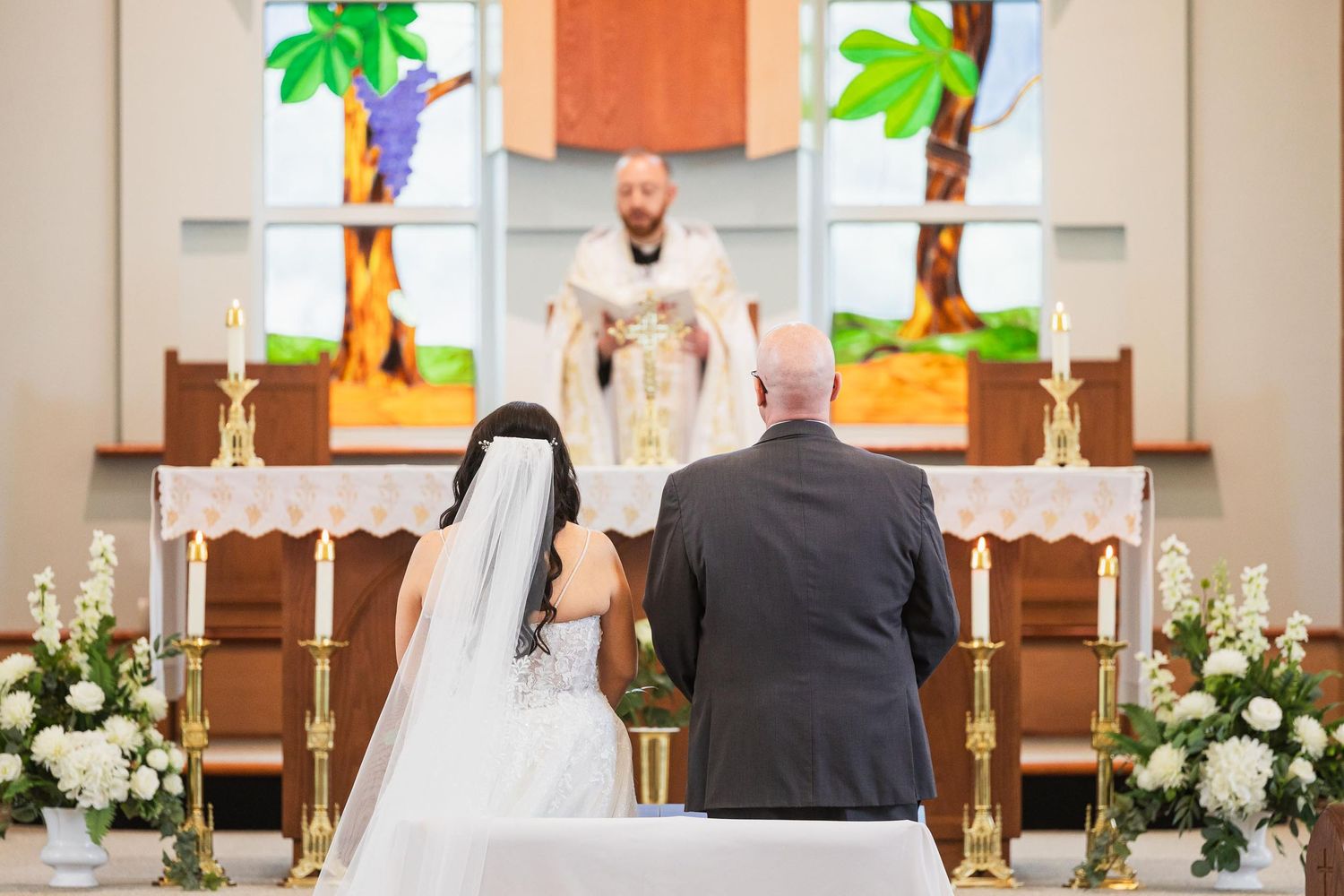 Wedding ceremony view from behind with priest officiating at decorated church altar.