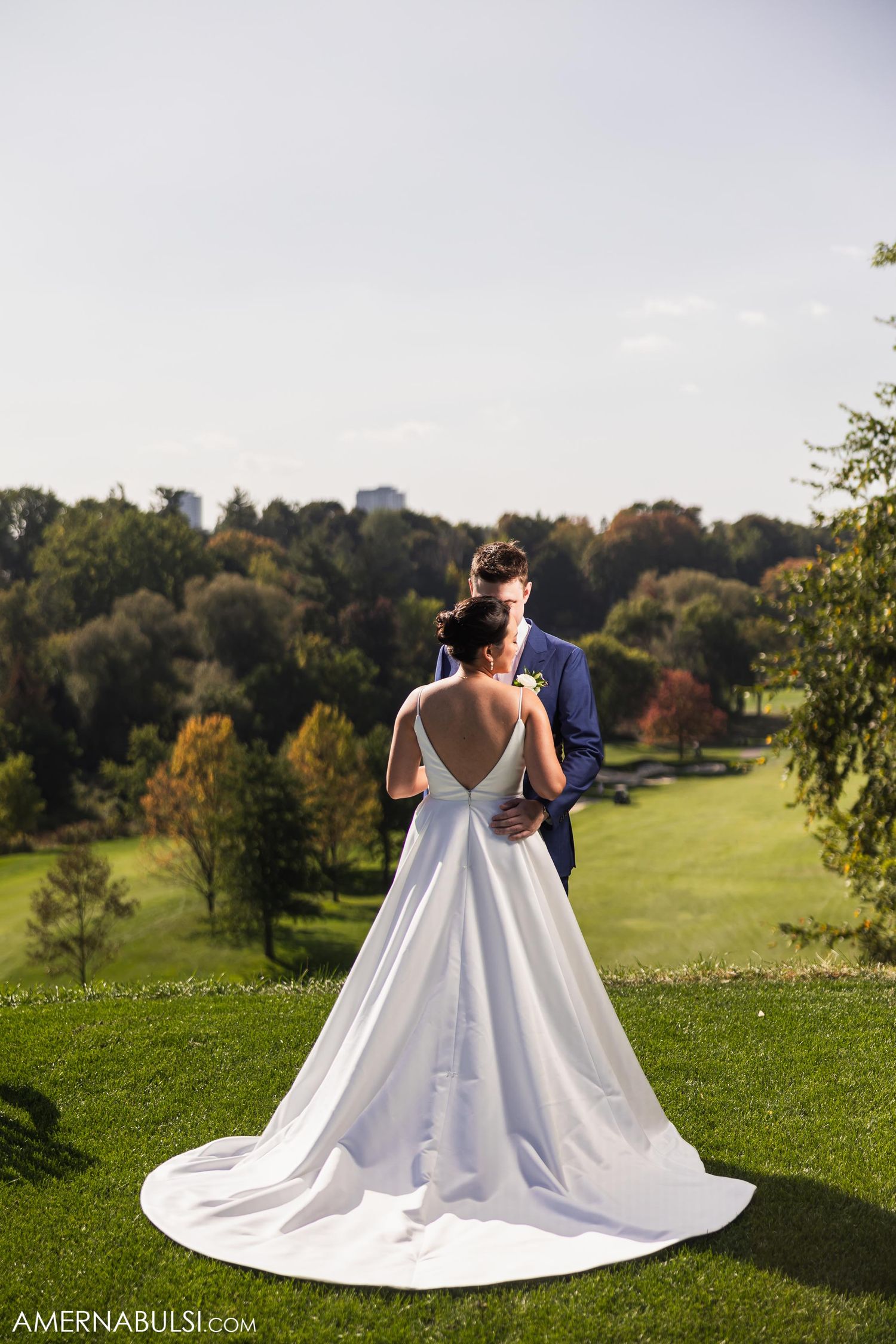 A bride in a white gown and groom share an intimate moment on rolling green hills.