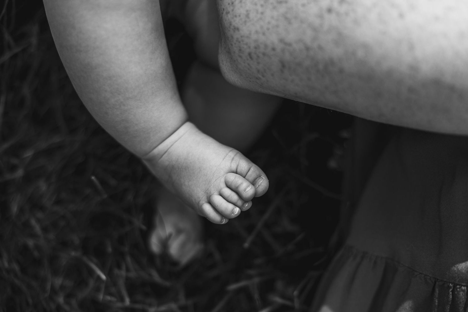 Black and white close-up photograph of small baby foot against dark background.
