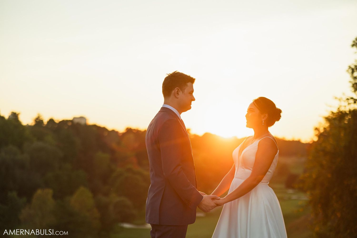 A couple shares an intimate moment at sunset in their wedding attire against a golden sky.