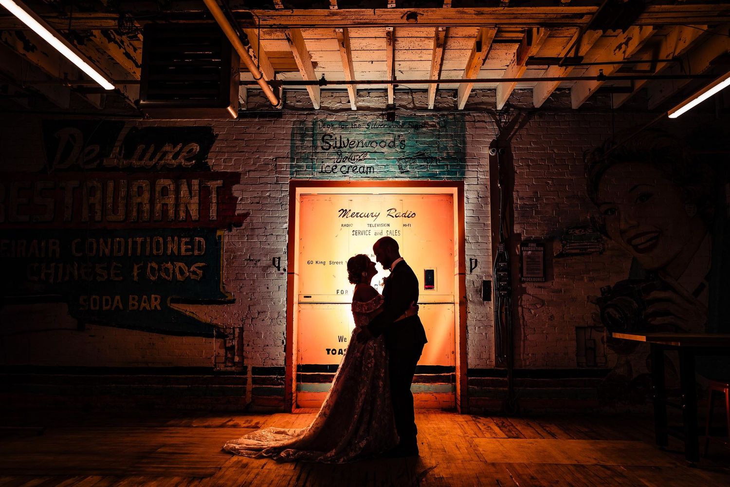 Silhouette of a couple embracing in front of a warm backlit doorway in an urban setting.