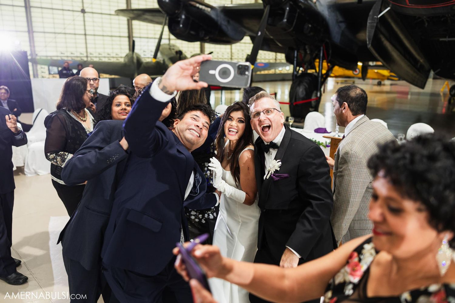 Wedding celebration group taking selfies together in aircraft hangar.