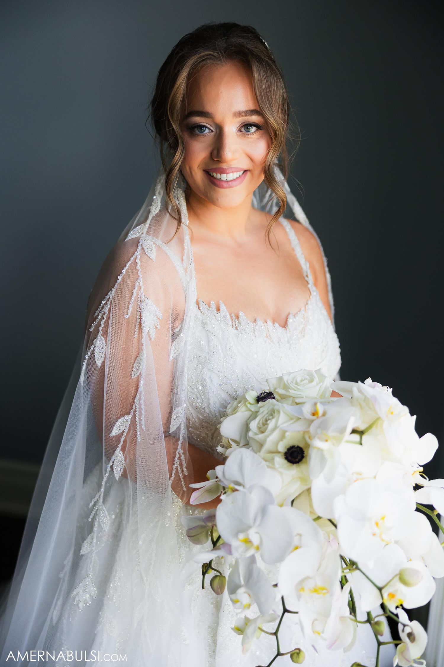 An elegant white wedding gown is paired with a stunning bouquet of white orchids and anemones.