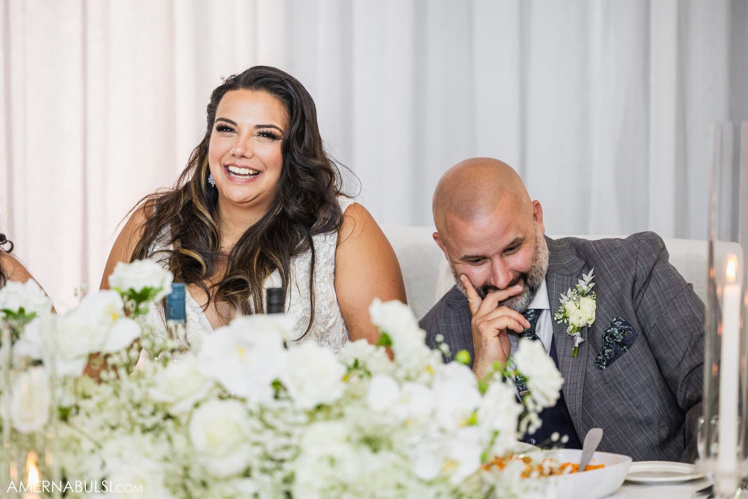 A couple sharing a candid moment at their wedding reception head table with floral decorations.