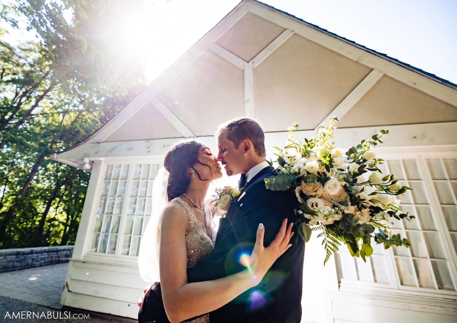 Sunlit wedding portrait in front of white chapel with beautiful lens flare effect.