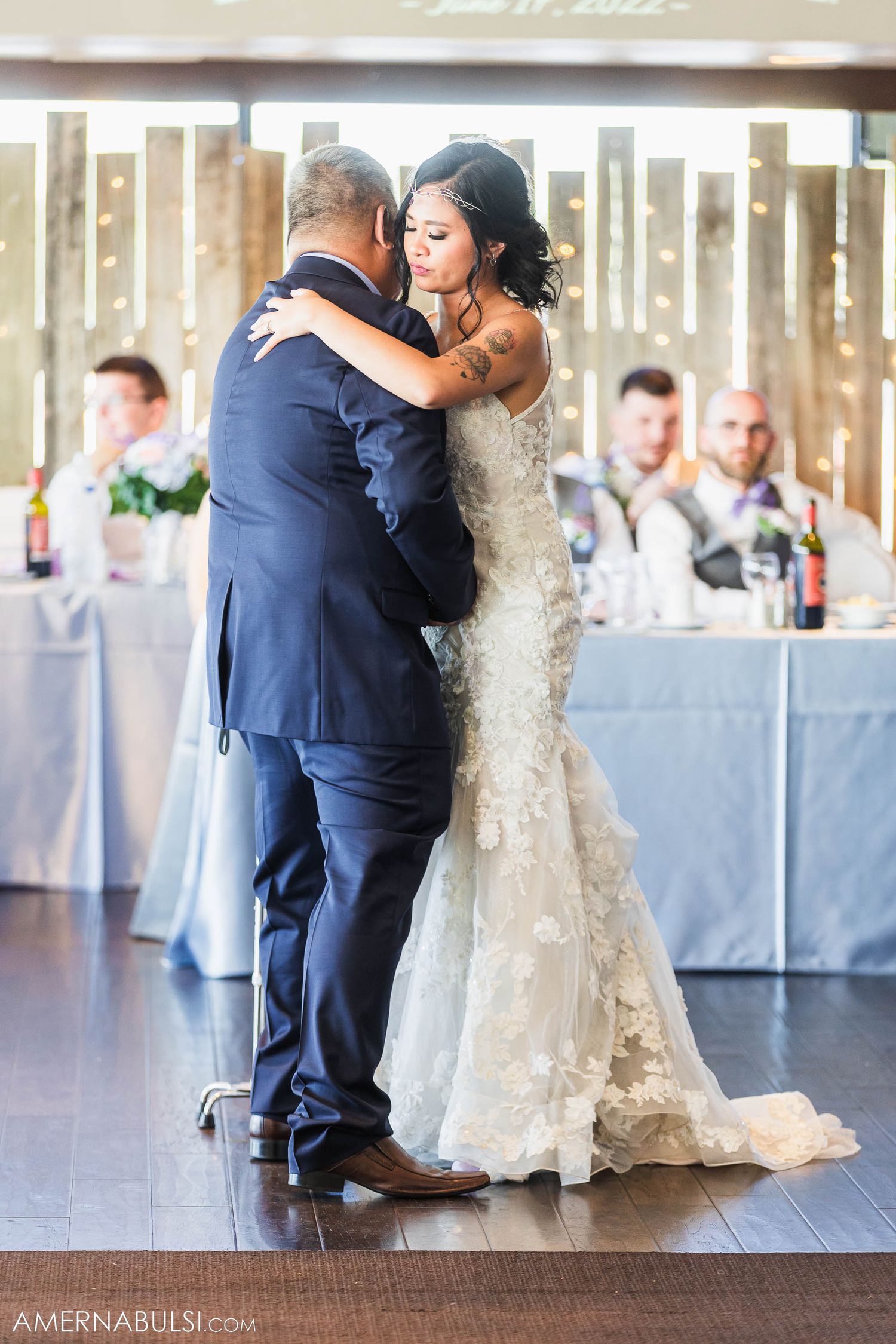 Couple sharing their first dance at a wedding reception with guests seated at tables in background.