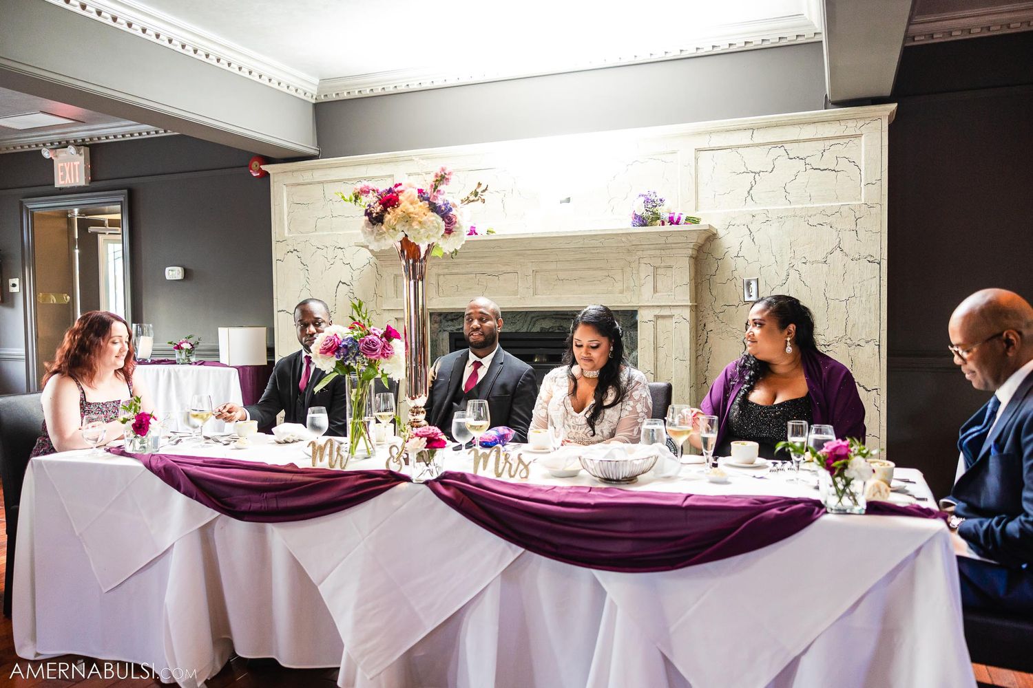 Wedding reception guests seated at elegant tables with purple sashes and floral centerpieces.