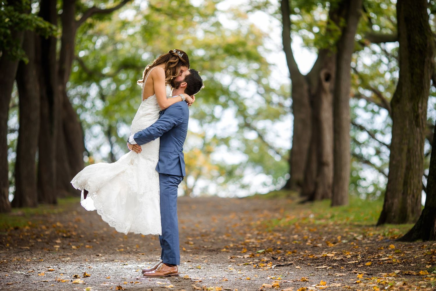 Autumn wedding photos captured on a tree-lined path with fallen leaves.