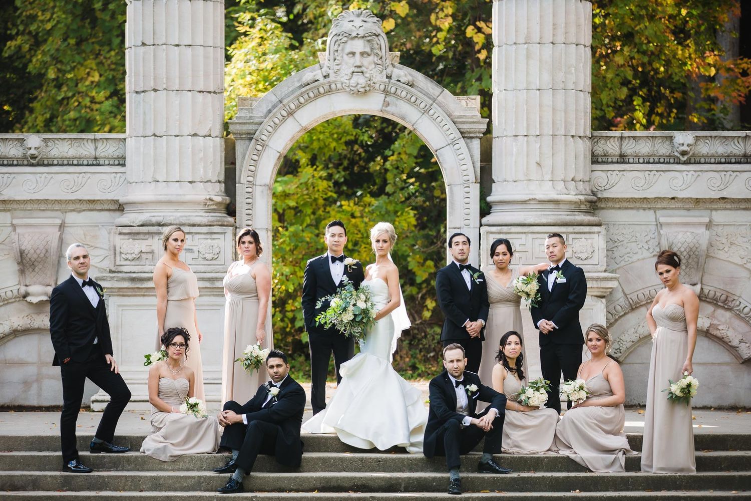 Classical stone archway and columns create elegant backdrop in formal garden setting.
