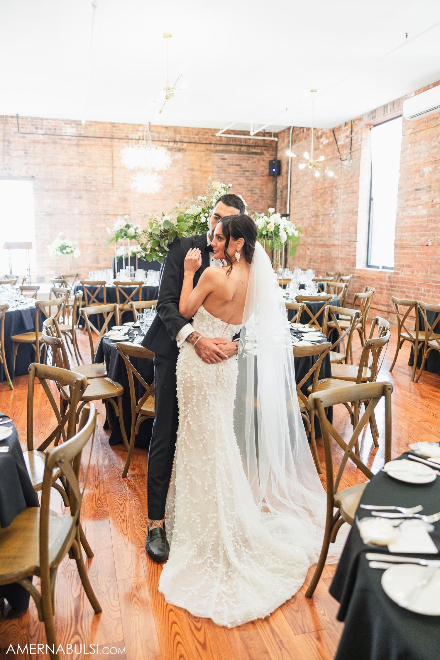 A tender moment between newlyweds in an elegant reception space with wooden chairs and exposed brick.