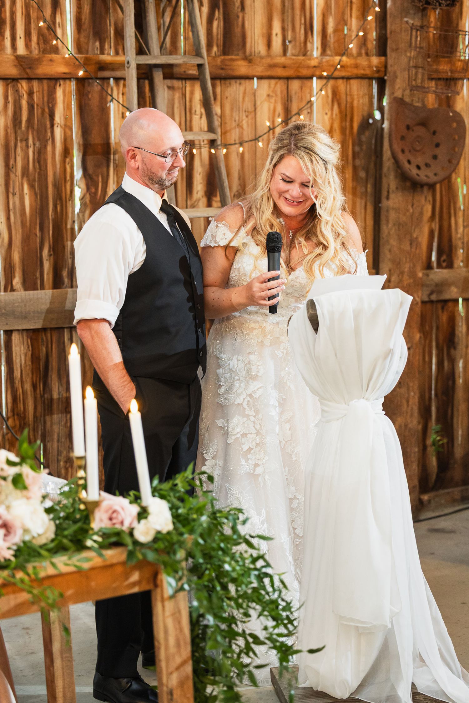 Wedding party and decor inside a rustic wooden barn venue with hanging greenery and elegant white draping.