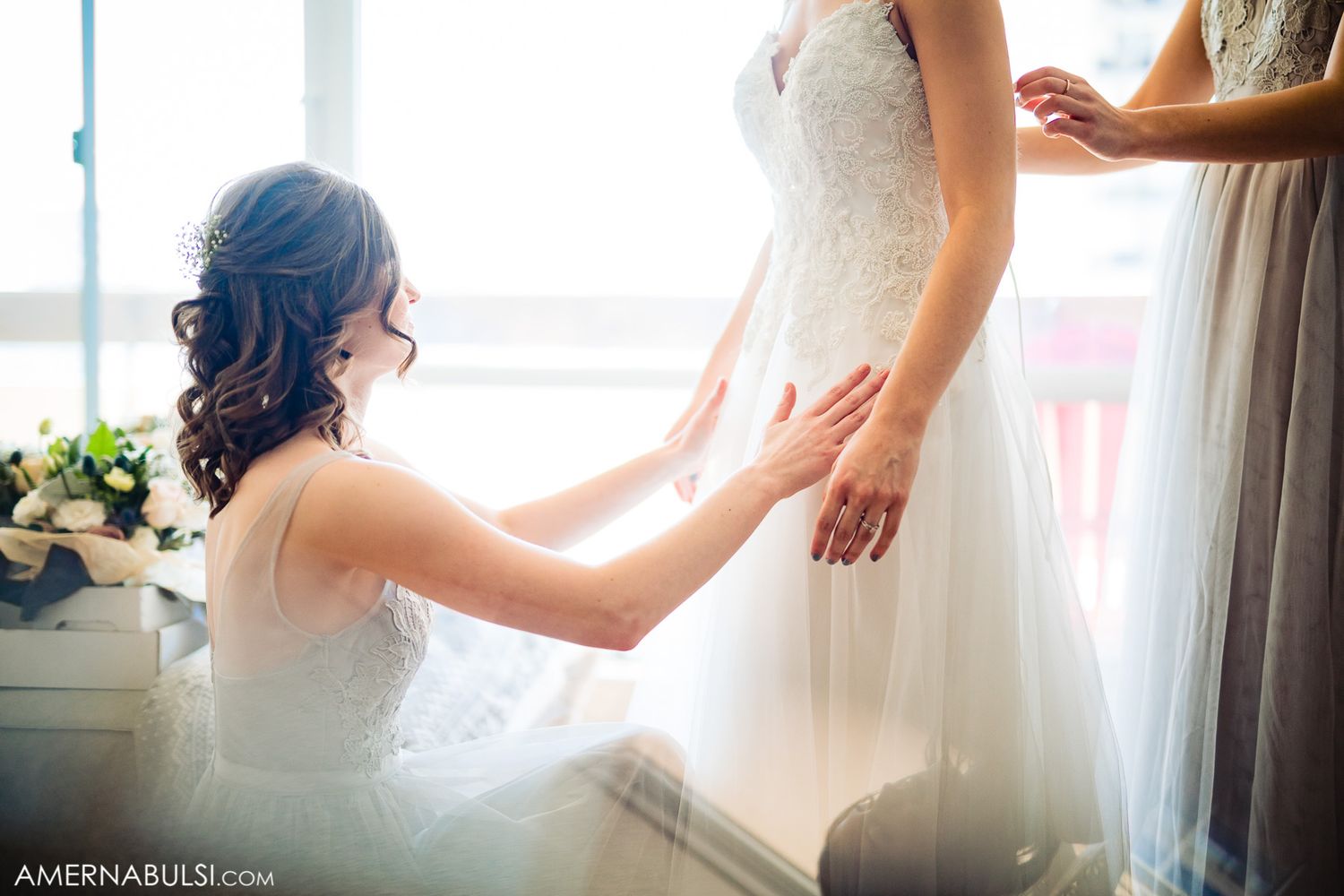 Soft natural light streams through windows as people prepare in flowing white dresses.