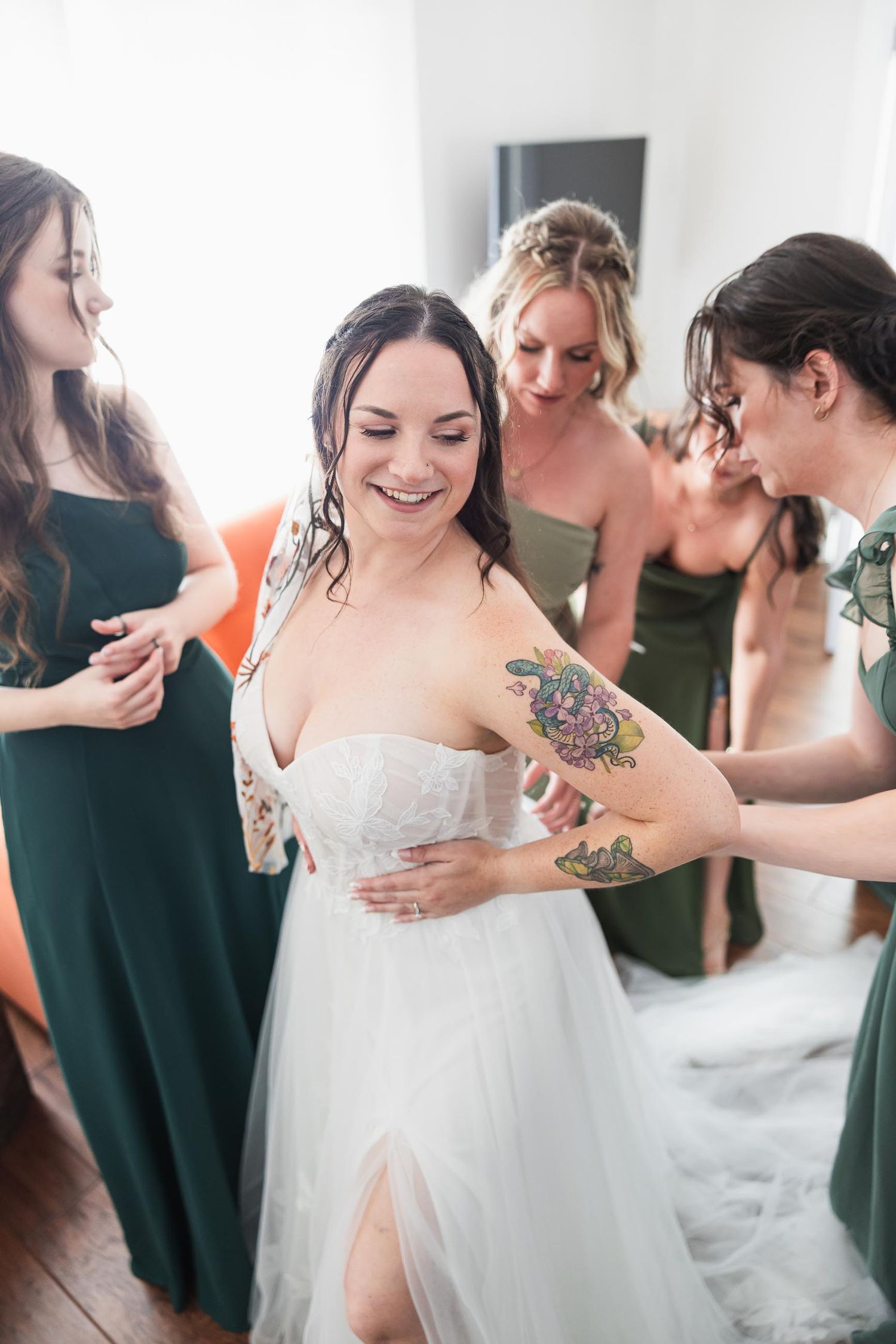 Getting ready scene with bride in white gown surrounded by bridesmaids in green.
