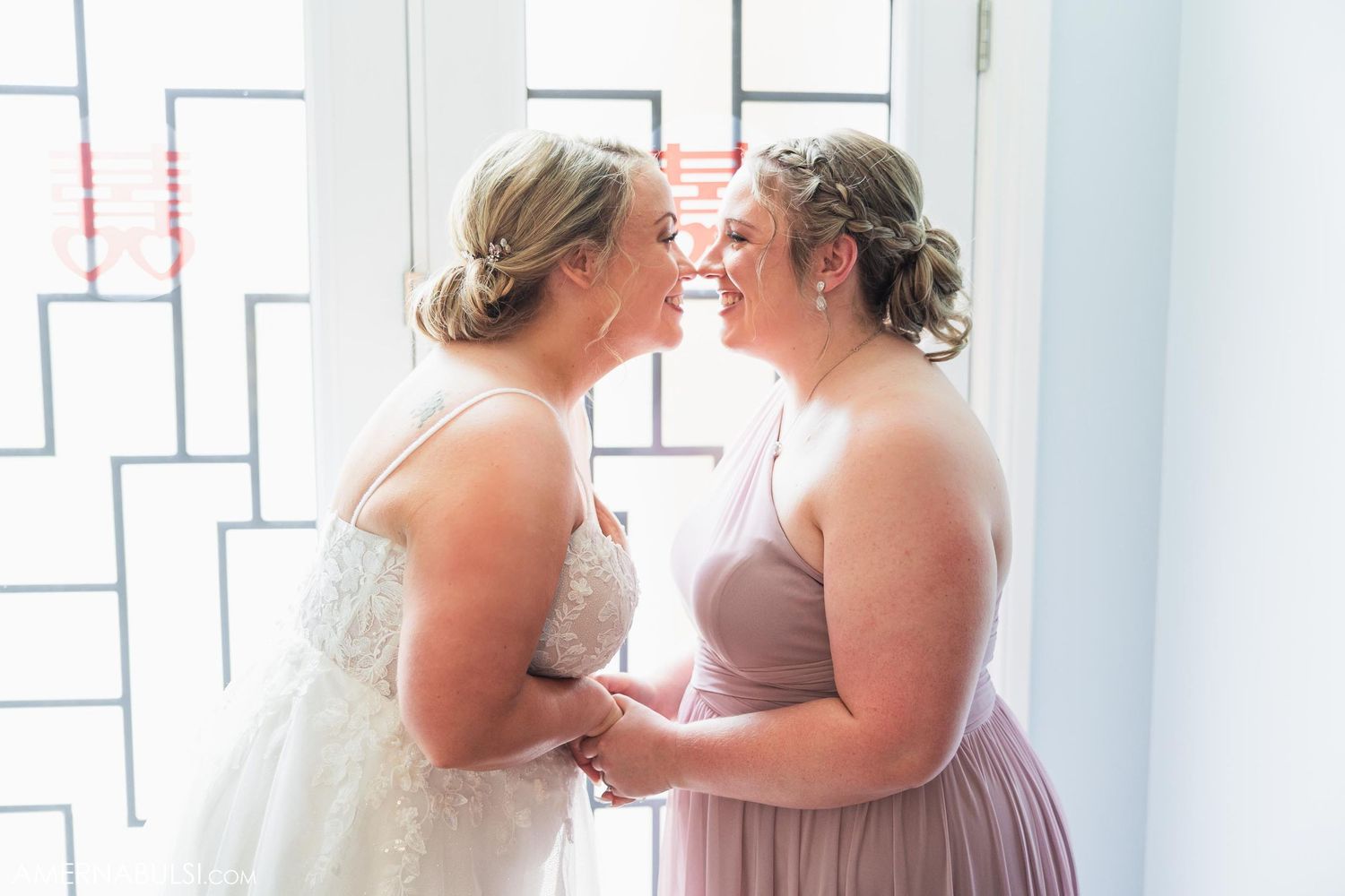 Two people in formal attire share a tender moment by a window with geometric patterns.