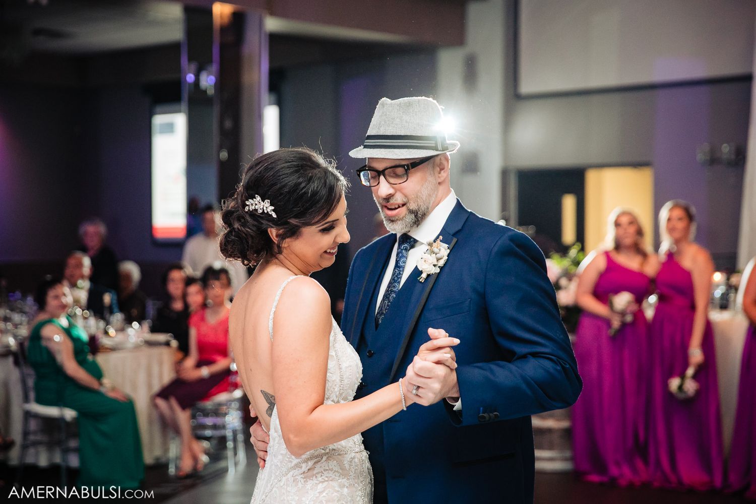 Panoramic view of a wedding reception venue with purple ambient lighting and dancing couples.