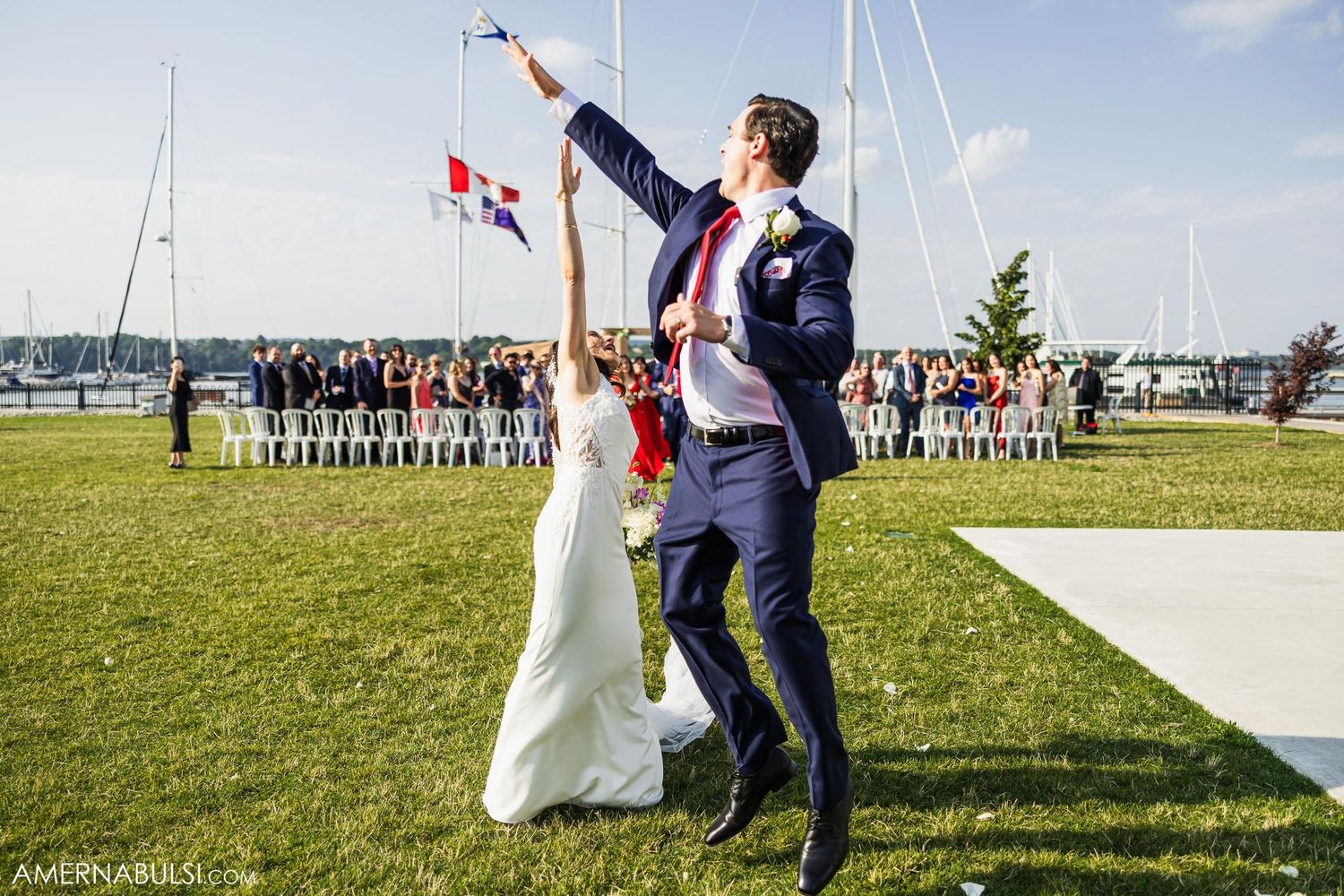Celebratory moment at waterfront wedding with flags flying overhead and guests in background.