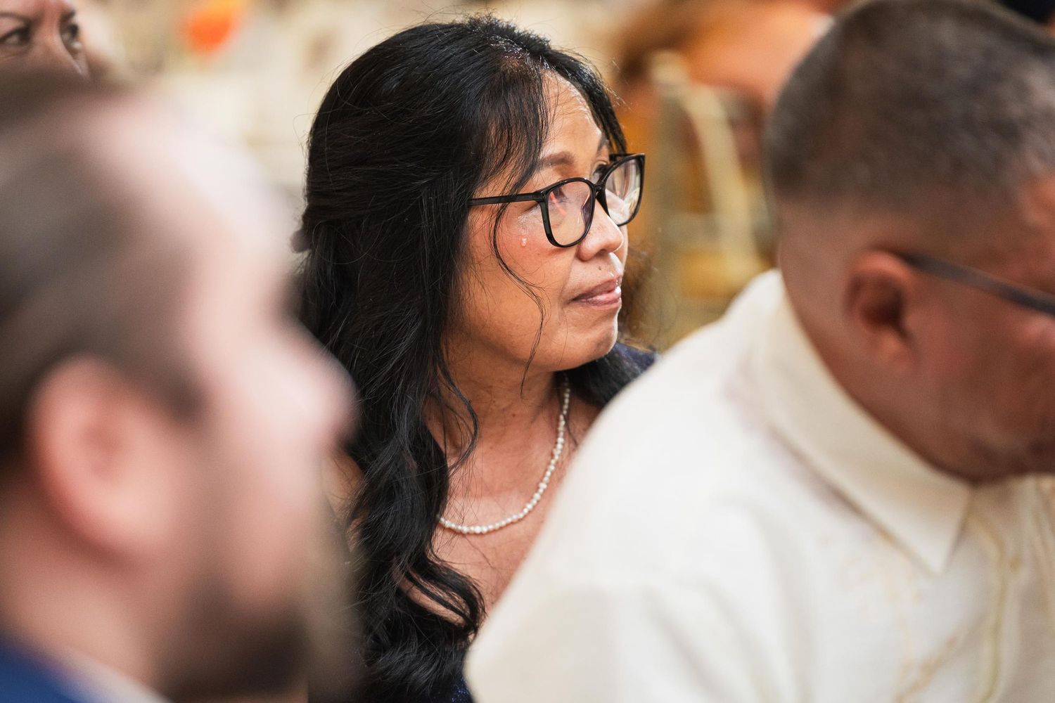 Guest wearing glasses and necklace listens intently during wedding reception.