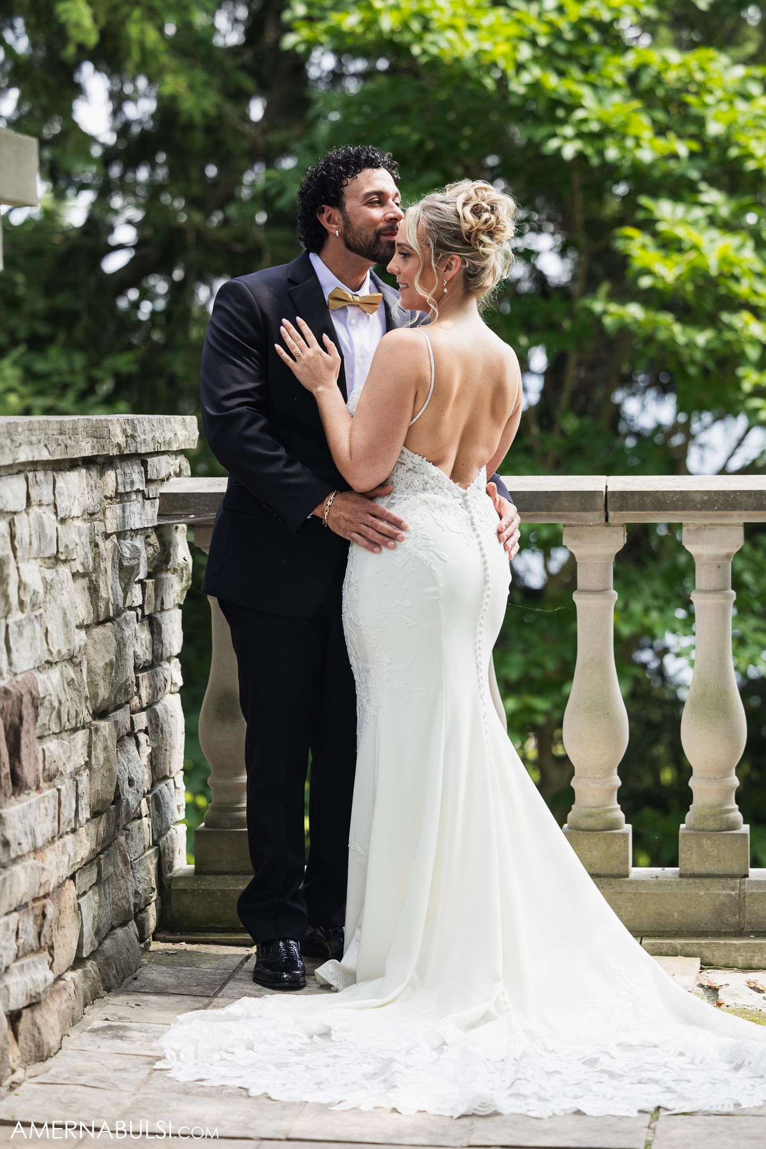 A romantic moment between newlyweds on a stone balcony with the bride wearing a lace train wedding dress.