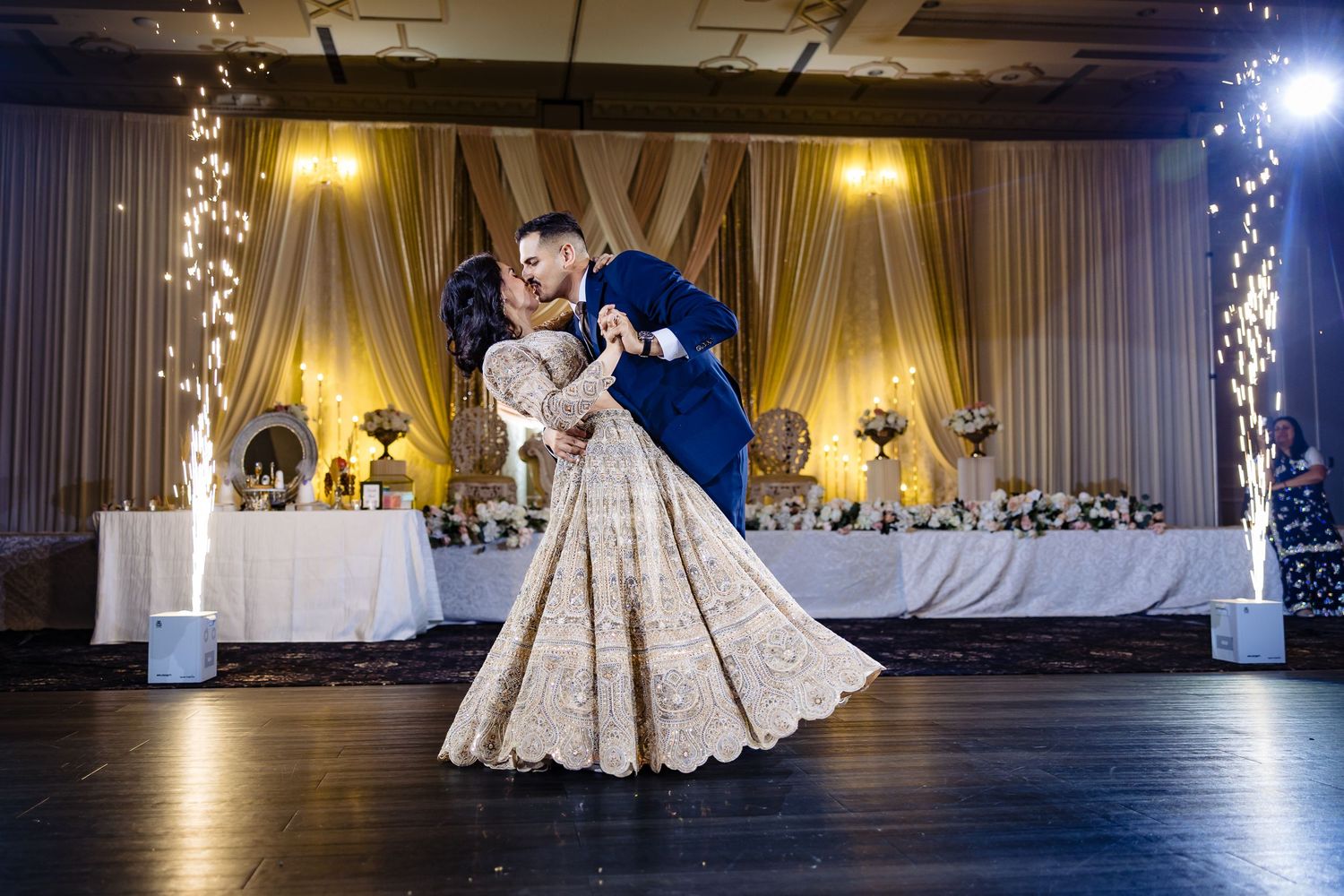 A couple dances in an elegant ballroom with warm lighting and decorative curtains in the background.