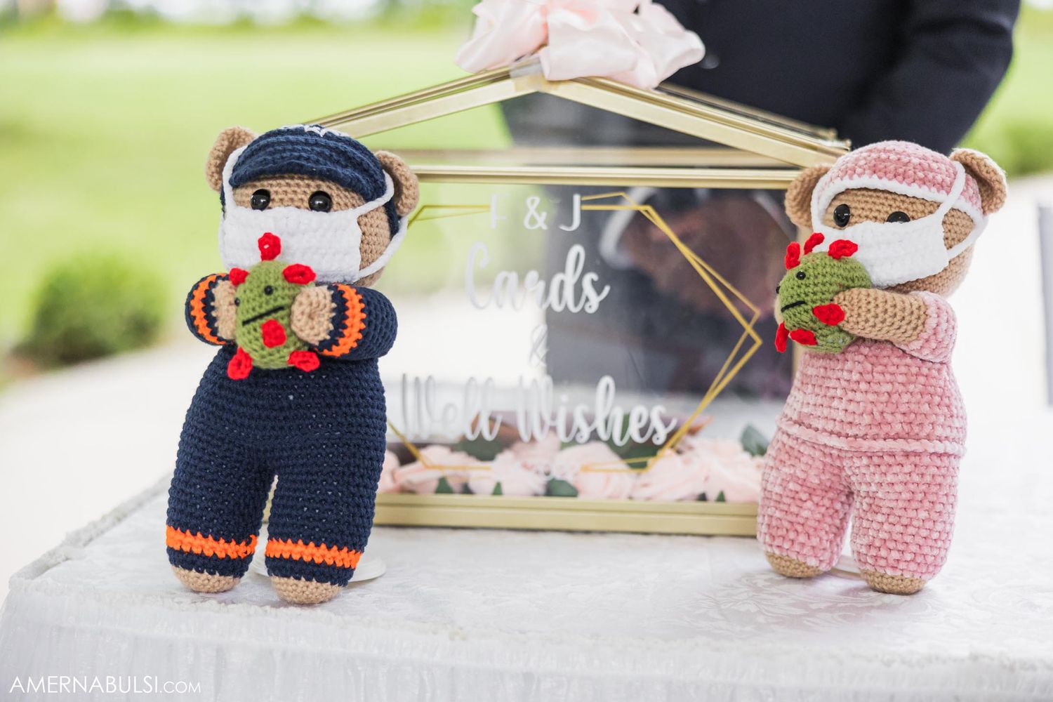 Two knitted teddy bear dolls in navy and pink outfits sit beside a wedding sign.