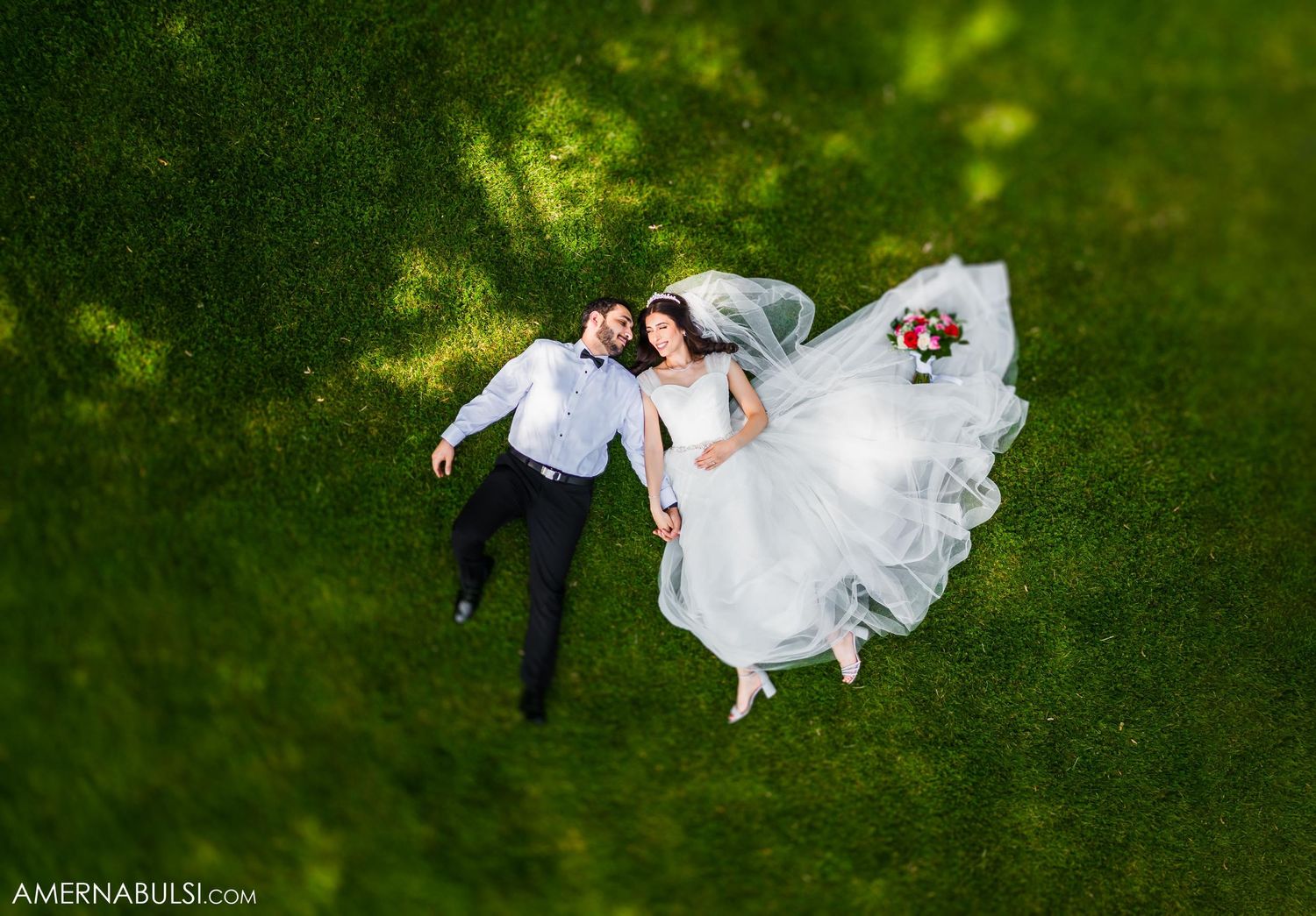 Aerial view of a couple lying on green grass during their wedding photoshoot.