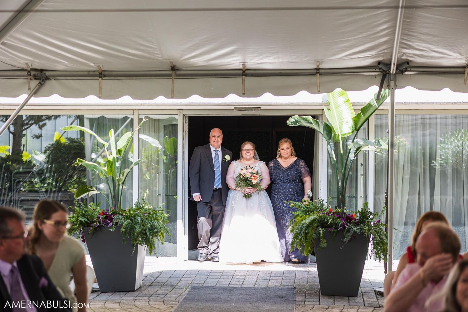 Wedding processional entrance through glass doors decorated with potted plants.