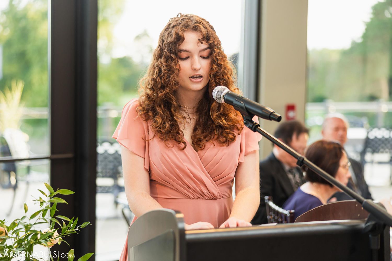Singer in pink dress performs at wedding with microphone and keyboard.