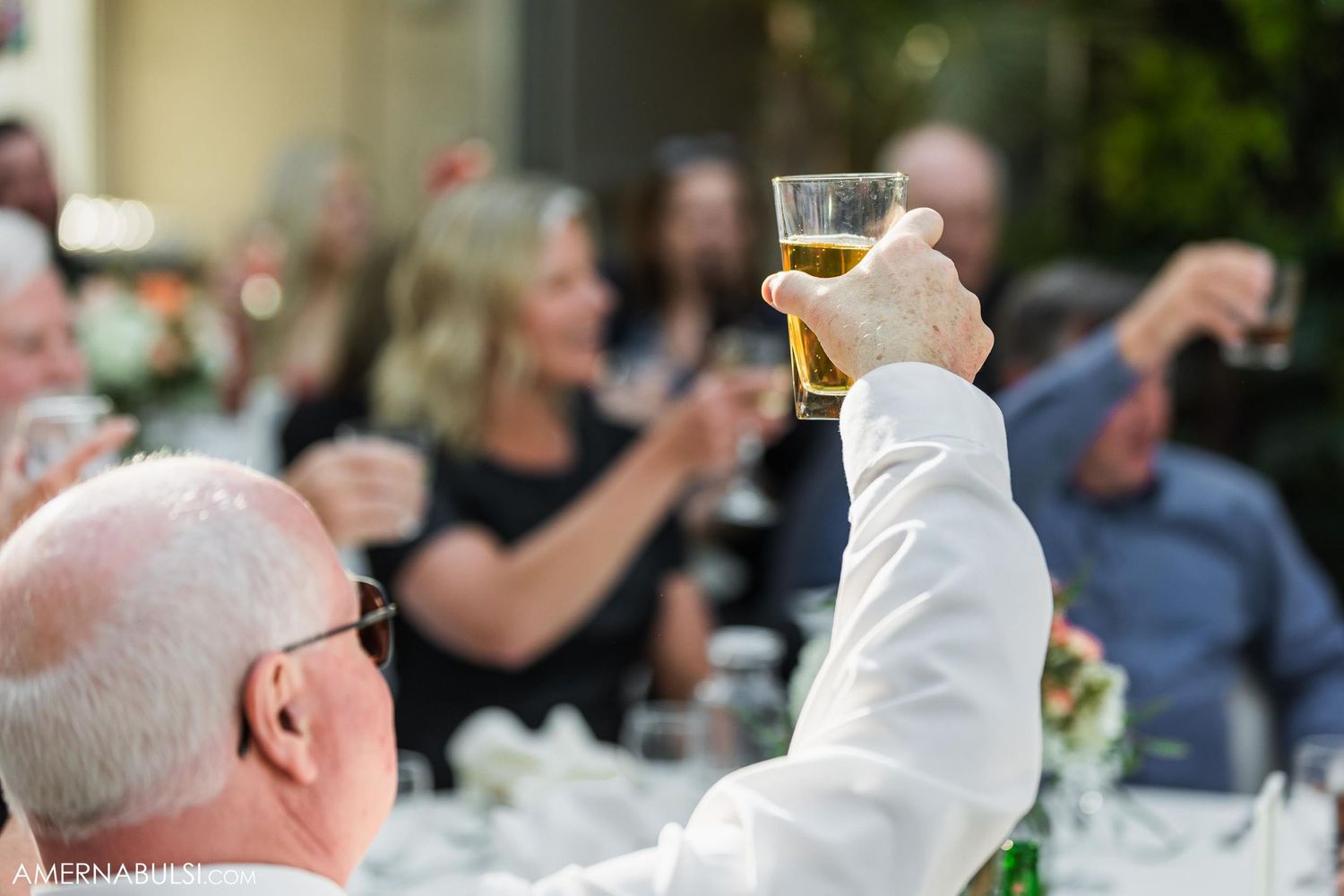 A wedding guest raises a champagne glass during a toast at an outdoor reception.
