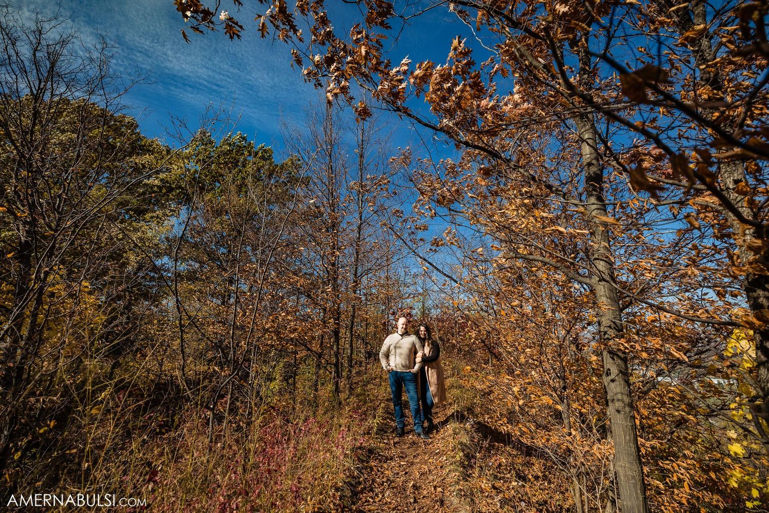 Couple walking along autumn trail surrounded by golden fall foliage.