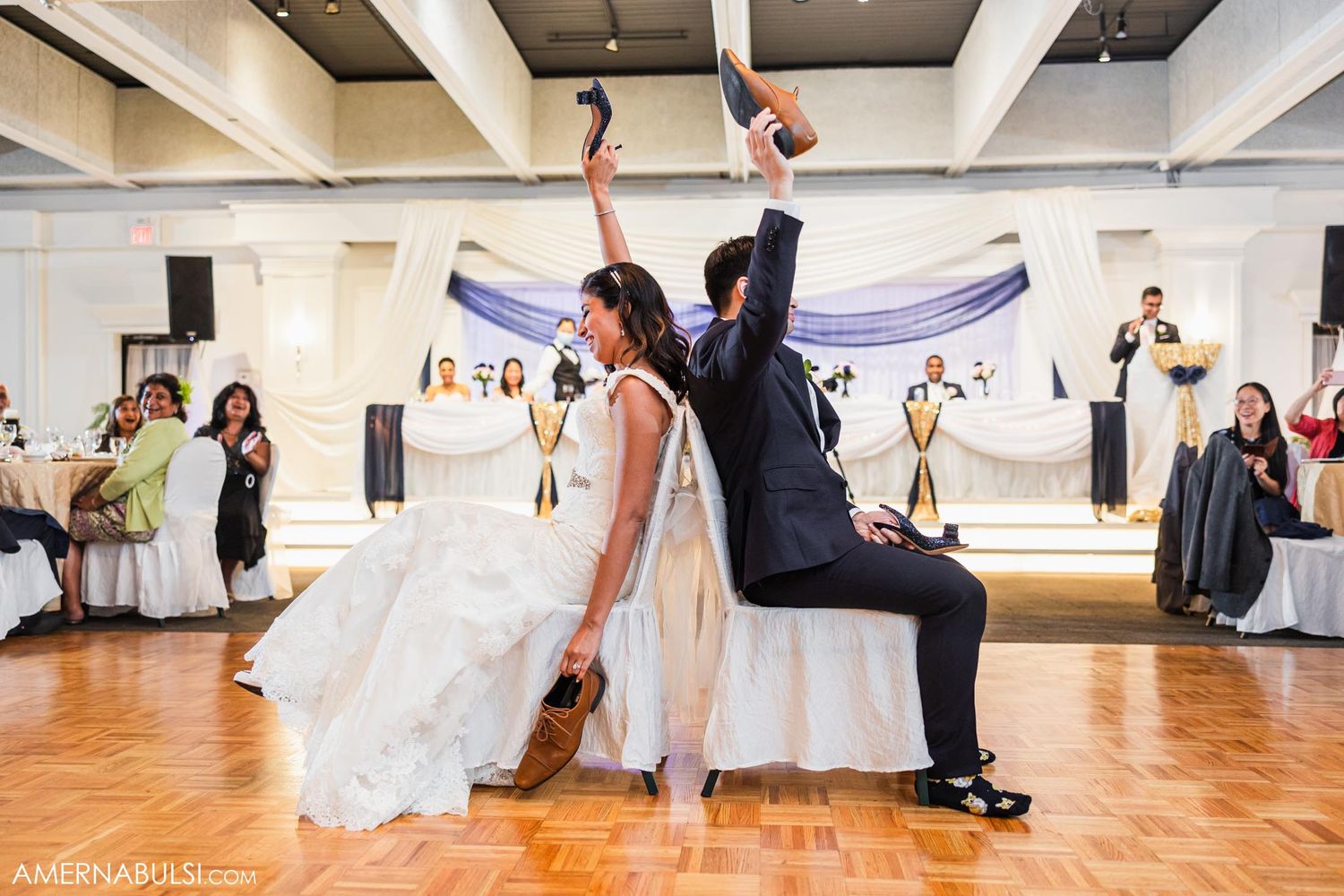 Newlyweds perform energetic dance moves during wedding reception on wooden dance floor.