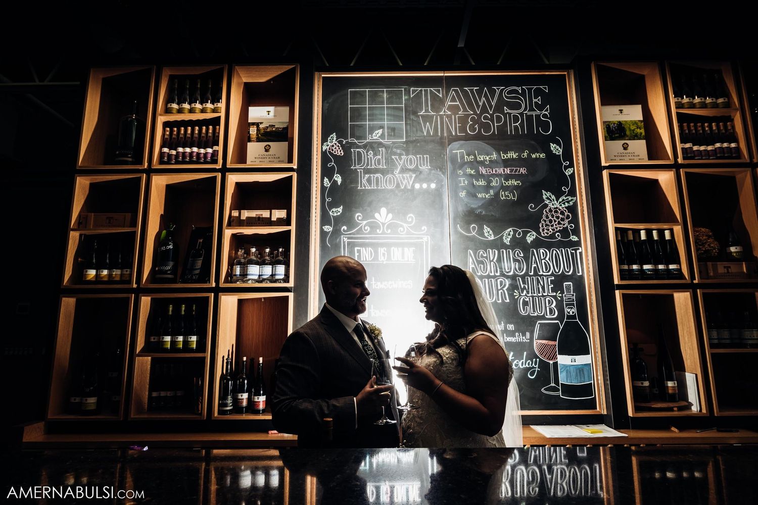 Silhouetted couple shares intimate moment against backlit bar shelving.