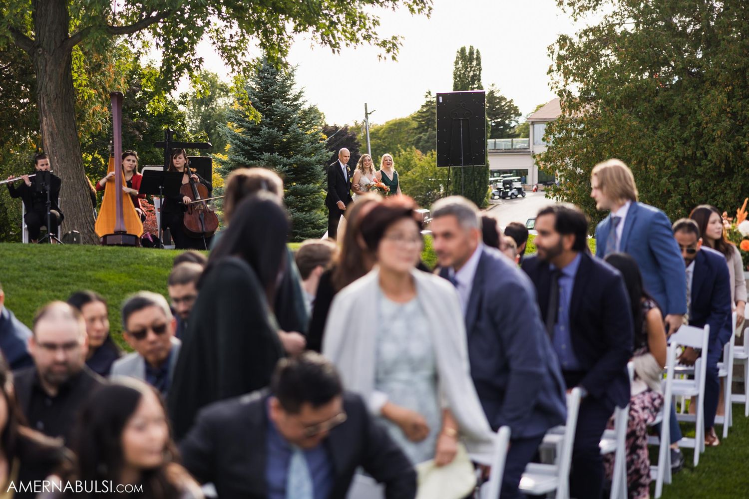 Wedding guests seated in white chairs during an outdoor ceremony at sunset.