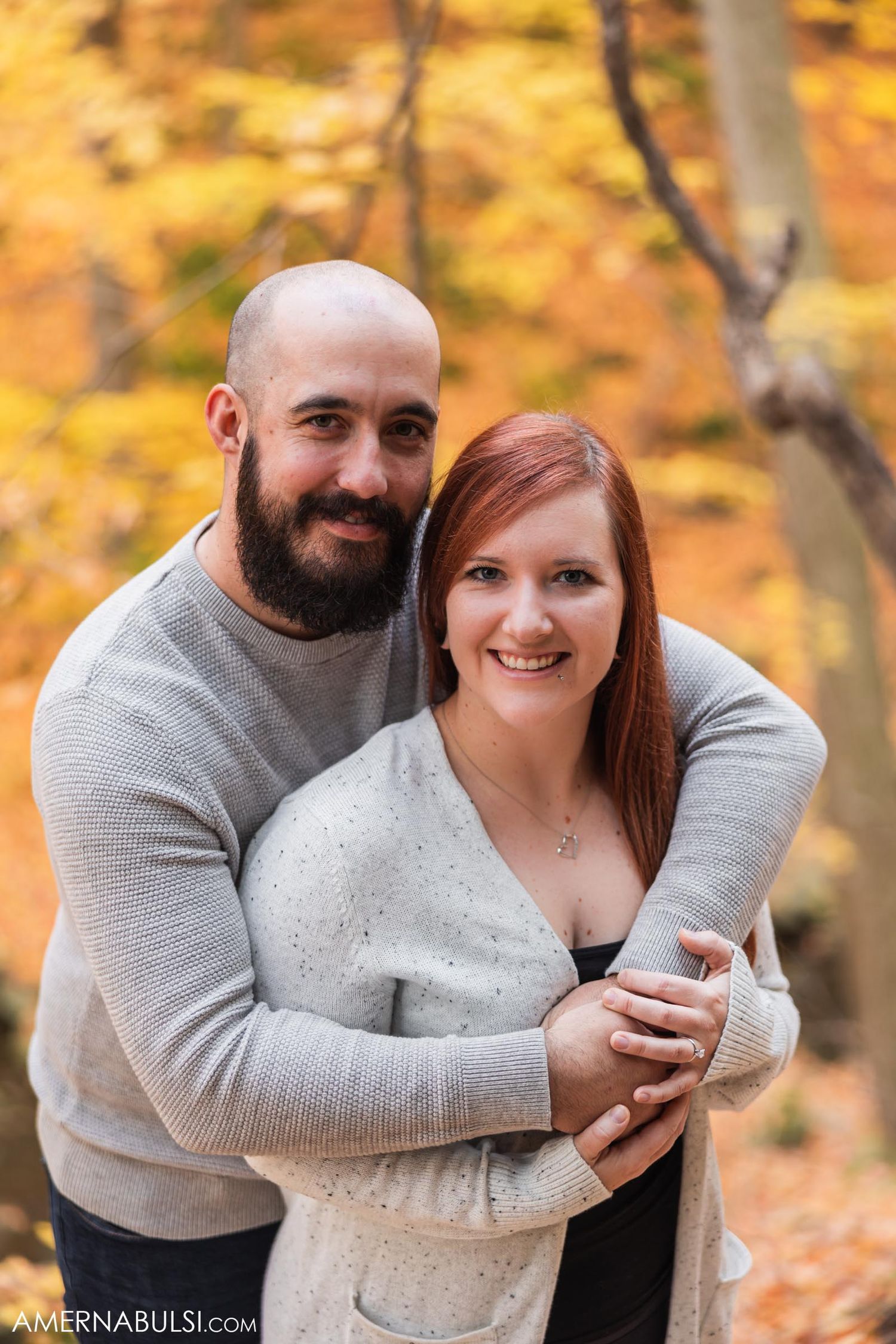 Happy couple embraces while surrounded by golden autumn leaves.