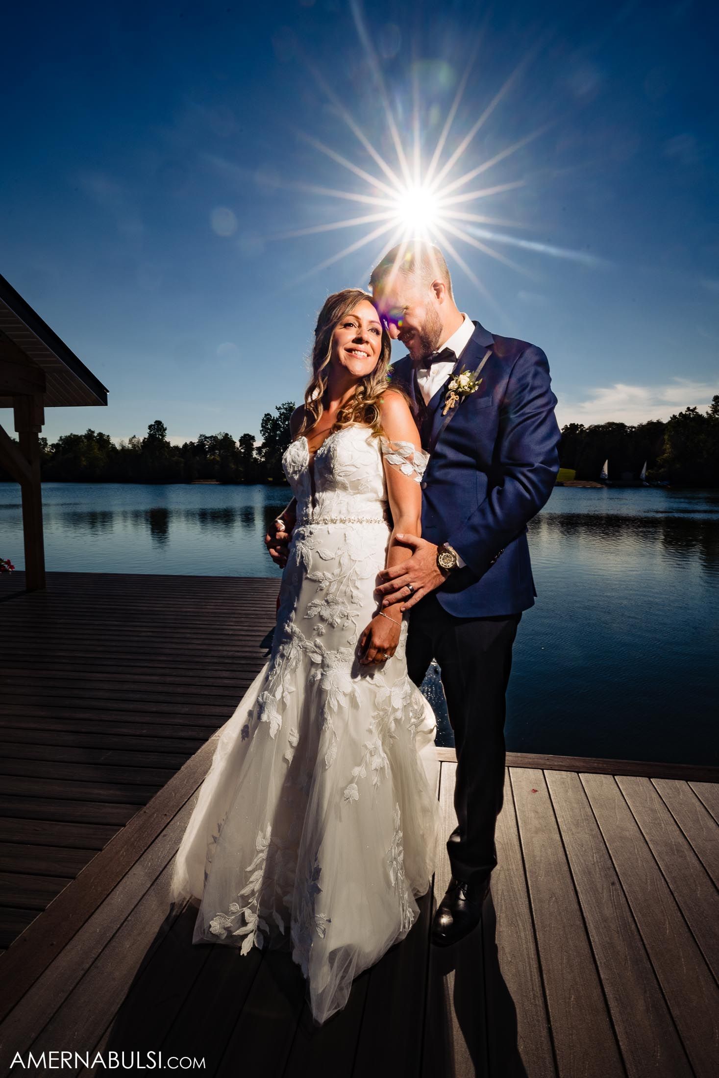 Stunning lakeside wedding photo with sun flare and reflection on wooden dock.