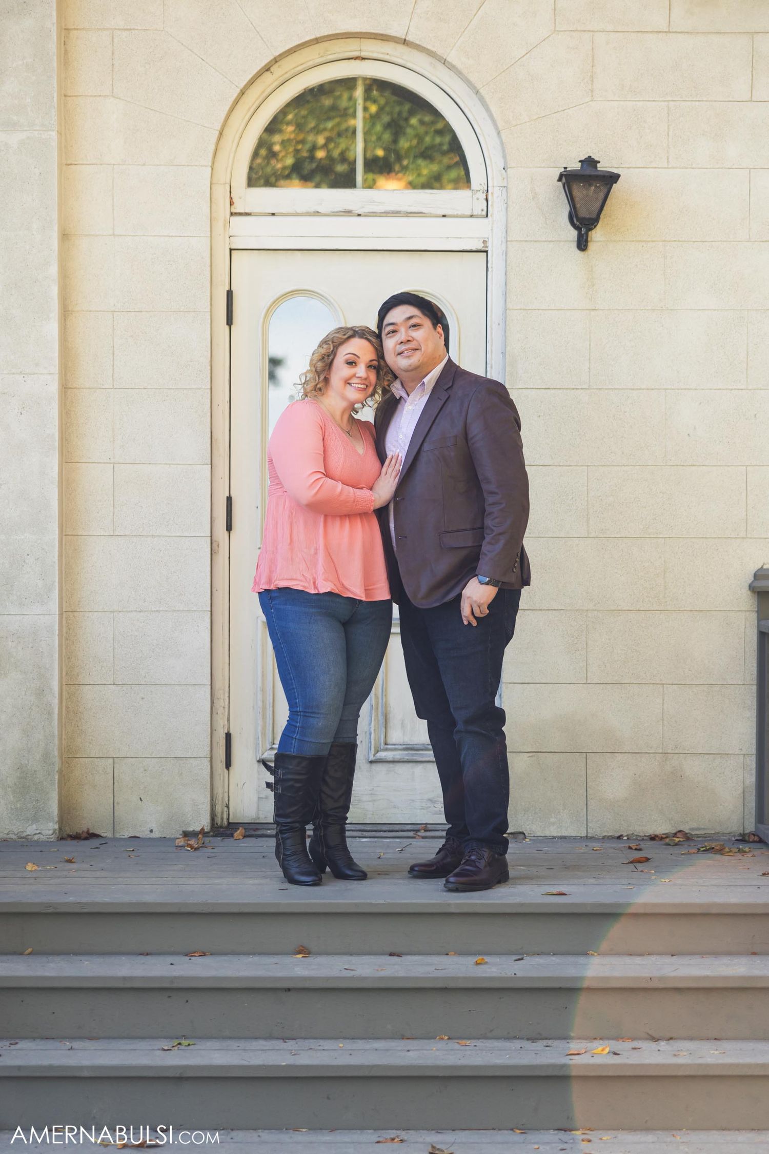 A couple poses together in front of an arched doorway of a historic building.
