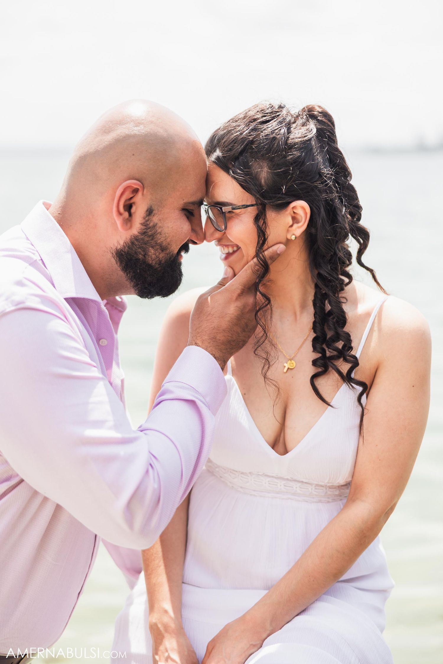 Romantic seaside moment between couple in white and pink attire.