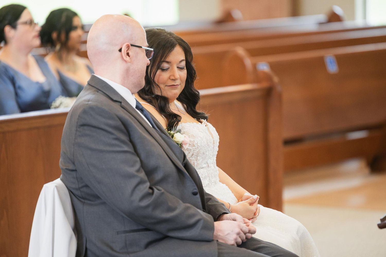 Wedding ceremony participants seated in wooden church pews during the service.