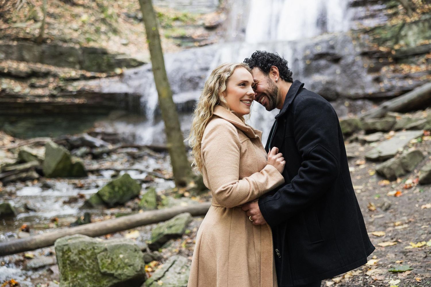 Couple shares an intimate moment in front of a scenic waterfall during autumn.