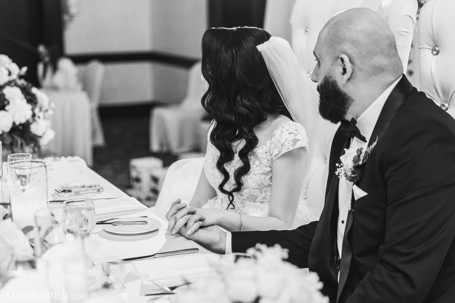 Black and white photo of couple sharing intimate moment at their wedding reception table.