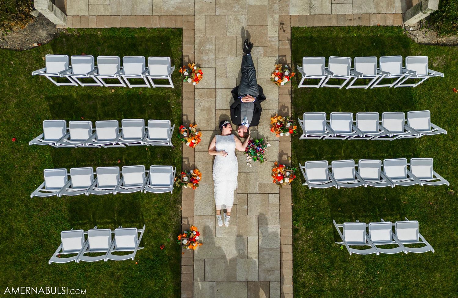 Aerial view of outdoor wedding ceremony setup with white chairs arranged symmetrically along stone pathway.