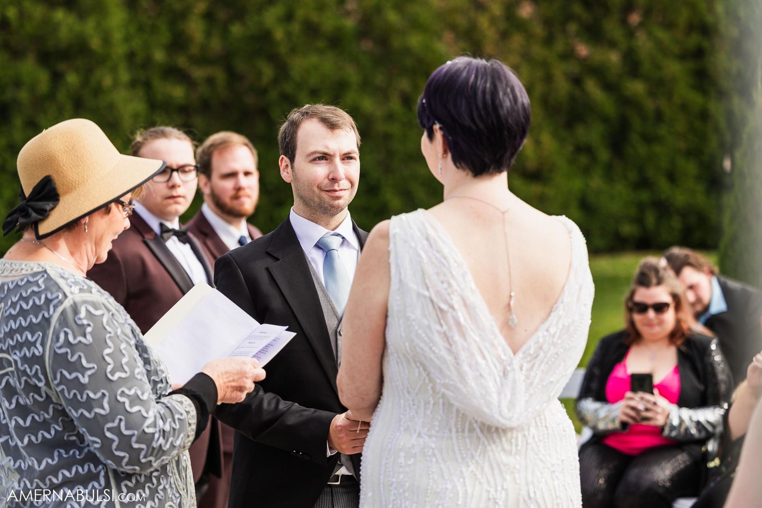 Outdoor wedding ceremony with guests watching as vows are exchanged.
