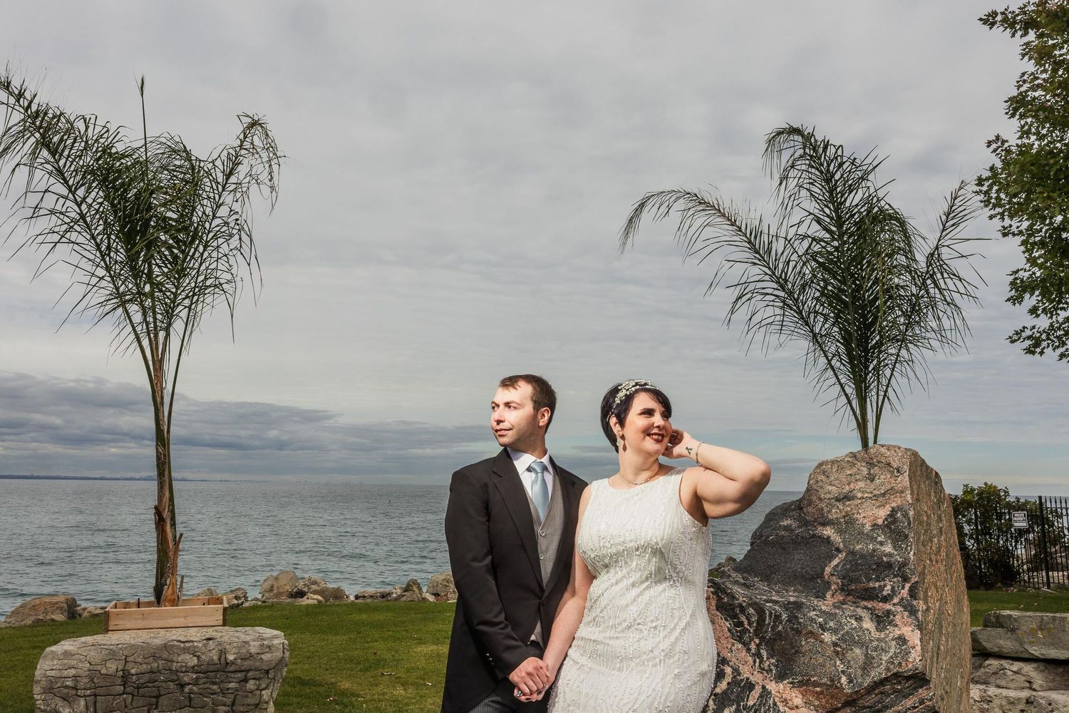 Seaside wedding portrait with palm trees and rocky coastline in background.