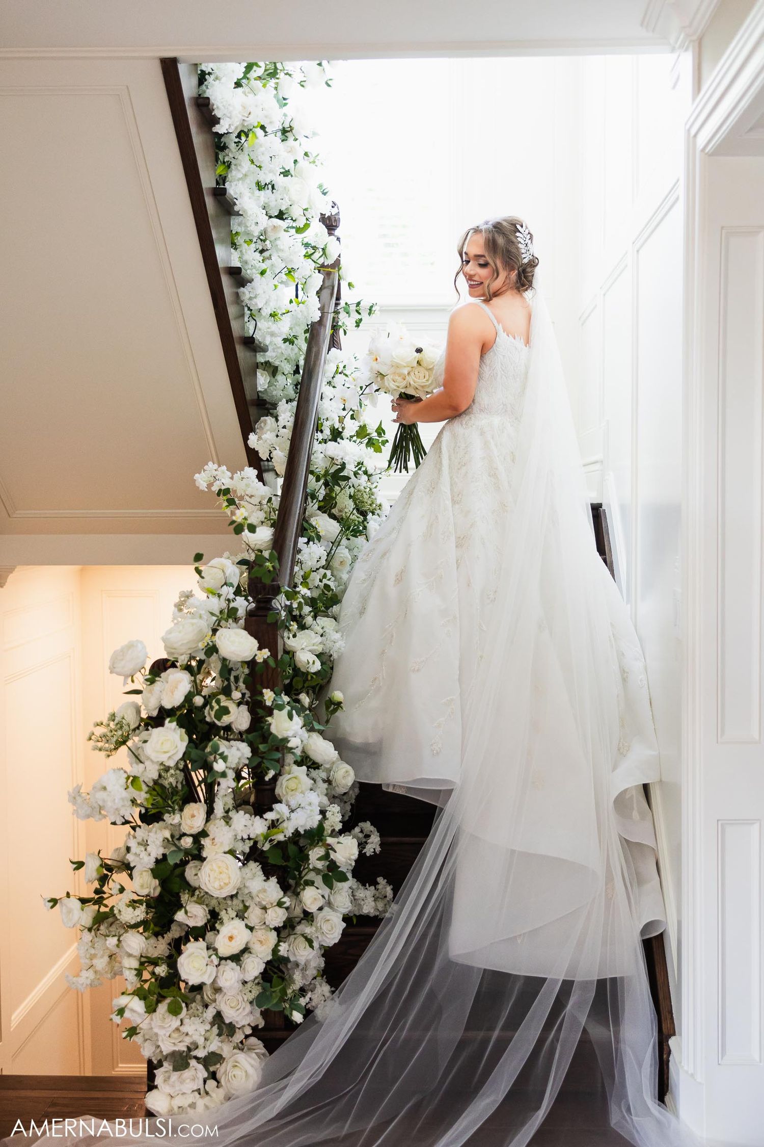 White floral arrangements adorn an elegant staircase while a flowing wedding dress creates a romantic silhouette.