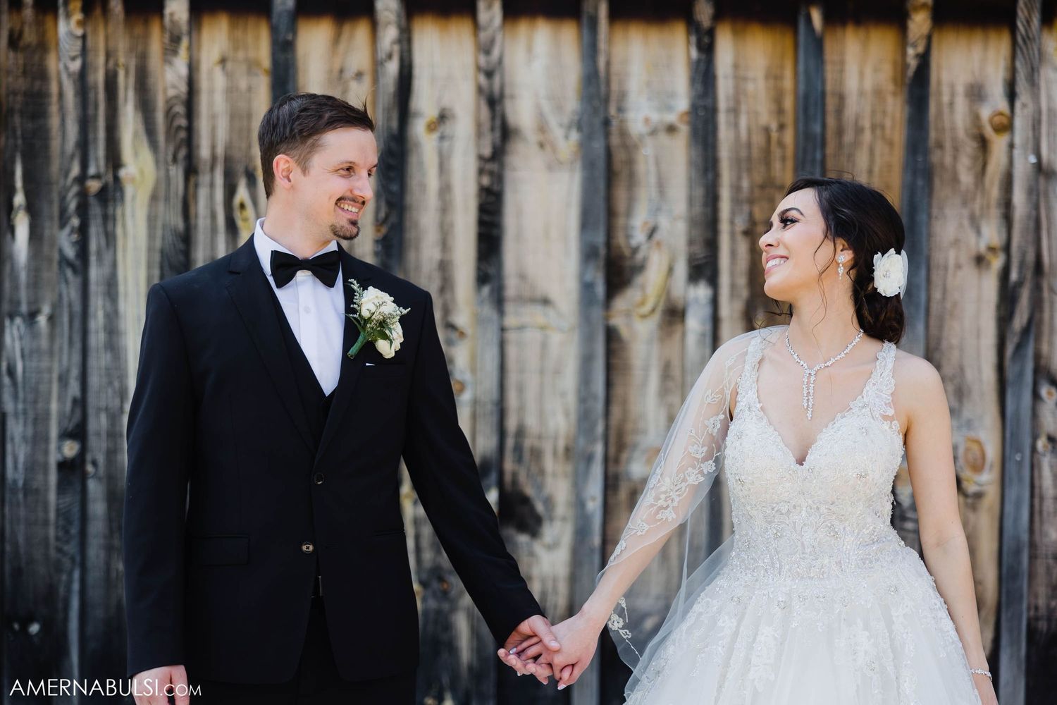 Newlyweds share a joyful moment together against a rustic wooden wall backdrop.