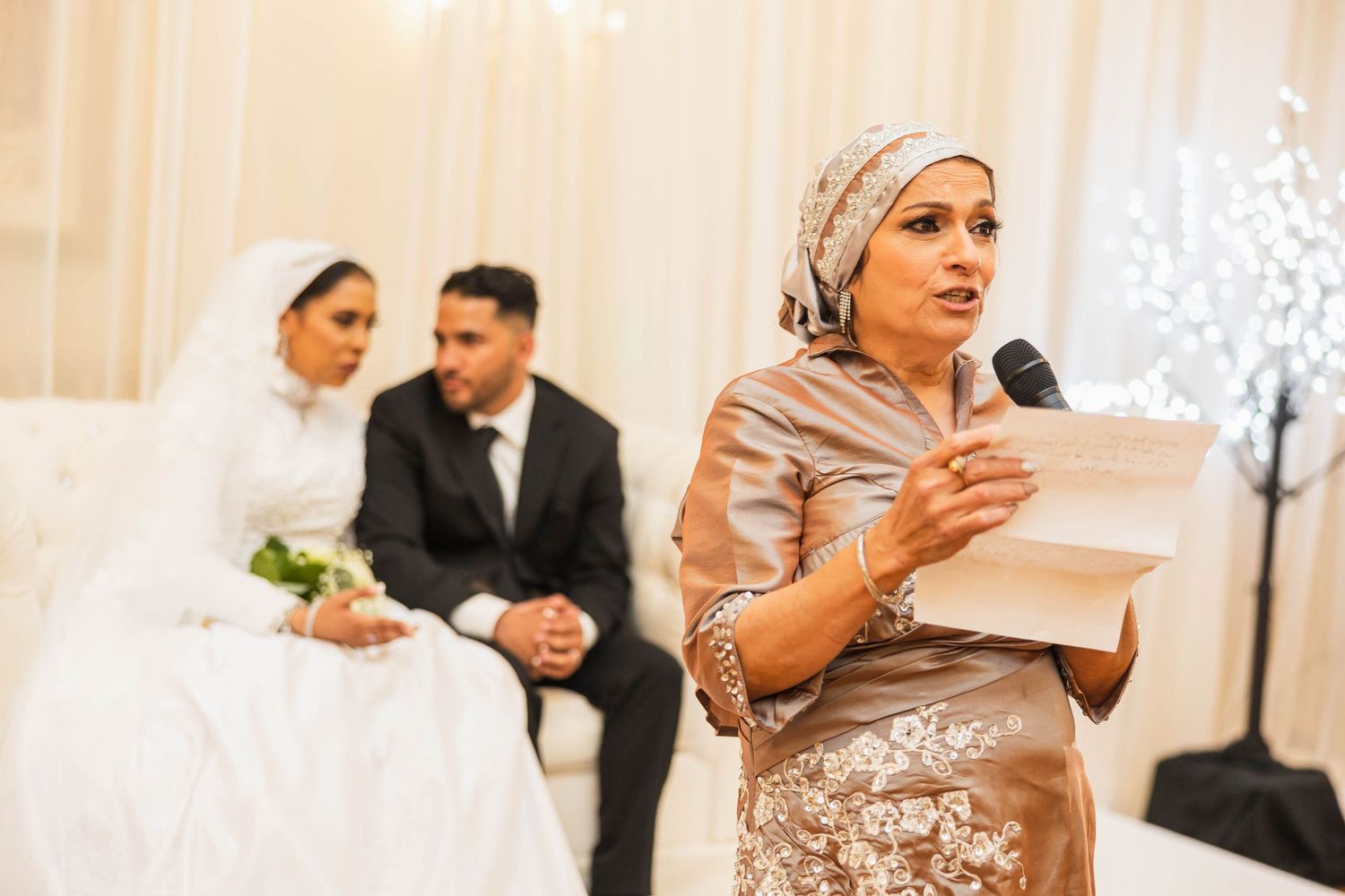 A speaker addresses wedding guests in an elegant reception hall.