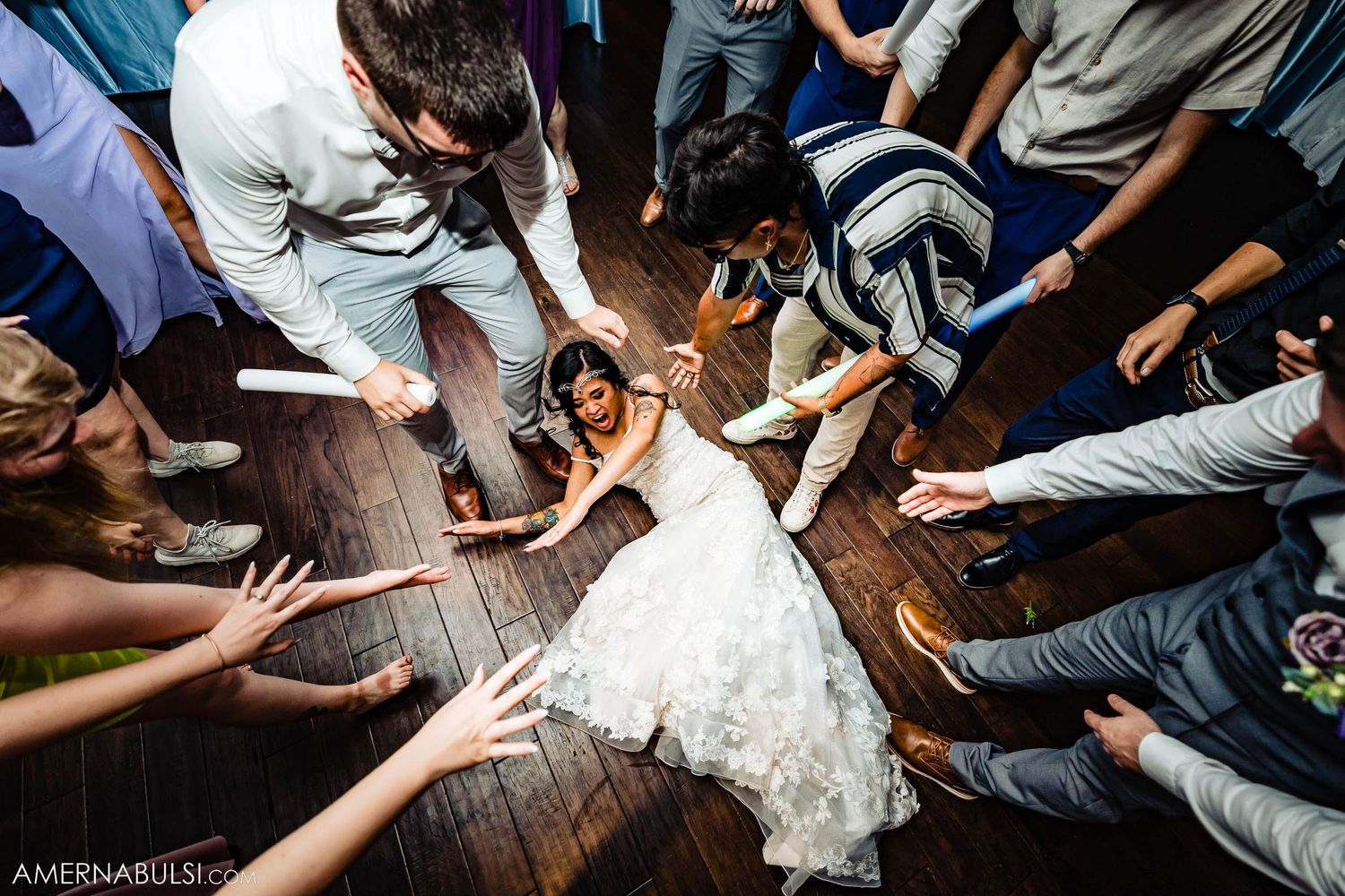 Aerial view of wedding guests dancing in circle around celebrating couple on wooden dance floor.