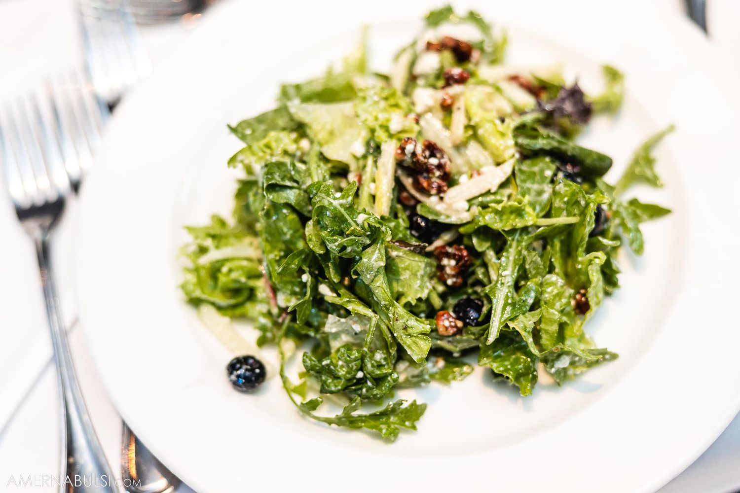 Fresh green salad with nuts and dried fruit served on white plate.