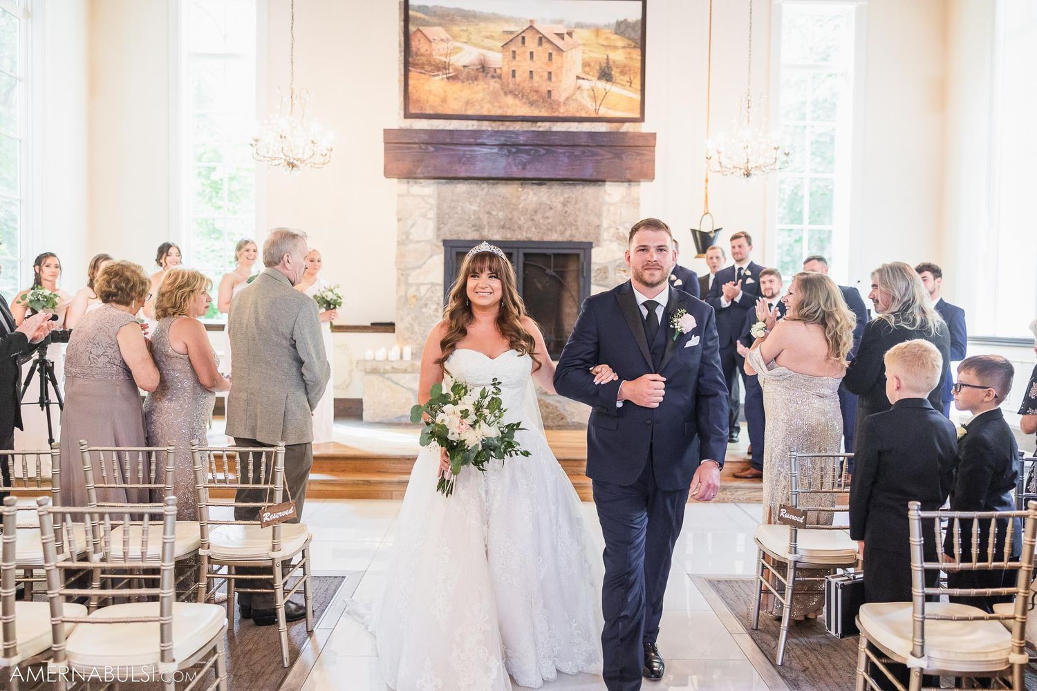 Wedding couple walks down aisle after ceremony in elegant venue with stone fireplace.
